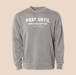 Gray sweatshirt with 'PRAY UNTIL SOMETHING HAPPENS' text on a beige background