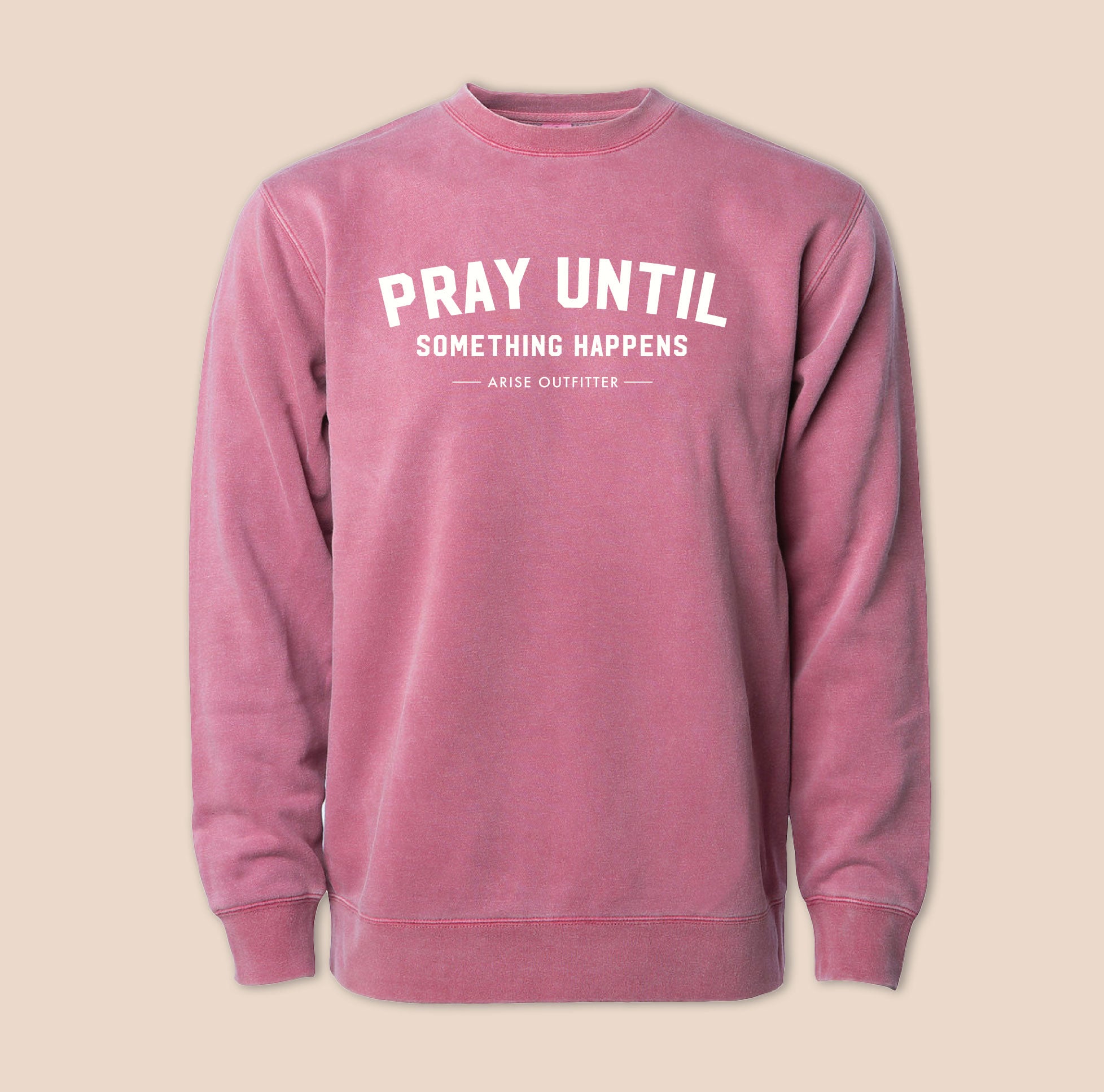 Pink sweatshirt with 'PRAY UNTIL SOMETHING HAPPENS' text on a beige background
